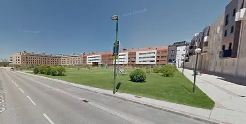 A park full of trees, bushes, green grass and some bakns to people rest and seat while children play around.,the camera can be seen looking down the street,auraria,street view,apartment buildings,osha