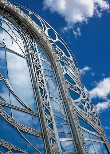 Modern architectural building, sleek silver aluminum extrusions, intricate framework, geometric patterns, reflective surface, urban cityscape, blue sky, white clouds, low-angle shot, dramatic lighting