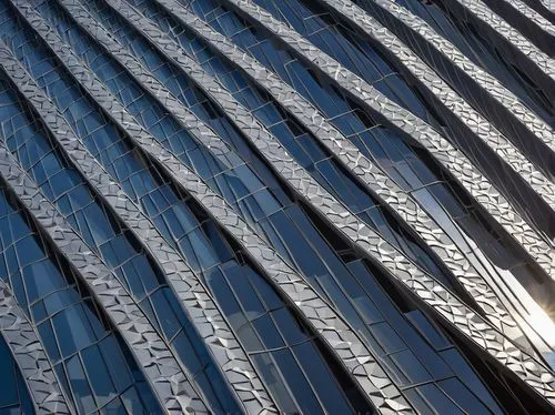 Modern building facade, architectural metal mesh, intricate patterns, silver-gray color, reflective surface, urban skyscraper, cityscape, sunny day, dramatic shadows, low-angle shot, 3/4 composition, 