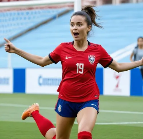 Same person wearing soccer cleats, soccer socks, soccer pants, bra. She scored a goal on a soccer pitch and celebrating by holding her red soccer jersey in her hand. she is running up the pitch near t