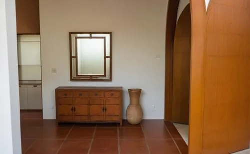 Entry way house in the woods, terra cotta floor, curved wood door, ceramic vase, rustic framed mirror, dark wood furniture,a bedroom with a dresser with mirrors and a cabinet,mudroom,home interior,hal