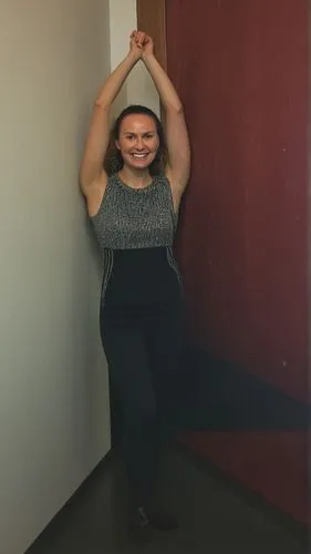 The discreet, young-at-heart lady stands proudly in front of a neutral gray wall, smiling and showing off her magnificent teeth and lush, curly hair.,half lotus tree pose,namaste,yoga,yoga pose,surya 