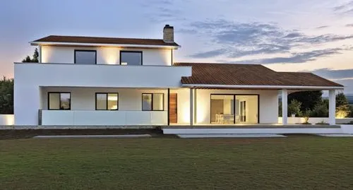 A modern, minimalist white house with clean lines and a few stone accents on the façade. The porch features white beams, complementing the sleek, minimalist design. The house is slightly elevated abov