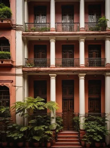 Residential building, Kolkata, Indian architecture, multi-story, red brick facade, white concrete pillars, ornate balconies, intricate iron railings, greenery-filled windows, wooden doors with carving