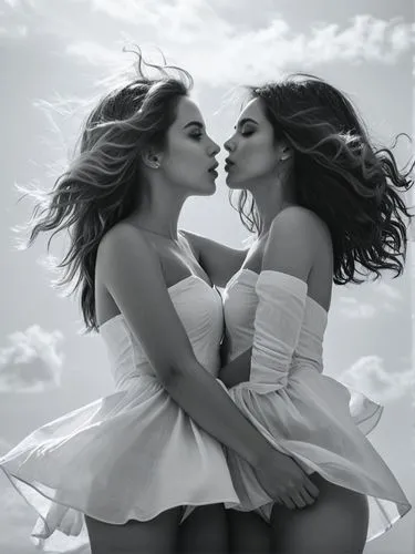 A black & white photo: The picture shows two young women facing each other and leaning close together, almost as if they were about to kiss. Both are wearing similar white, off-the-shoulder dresses th